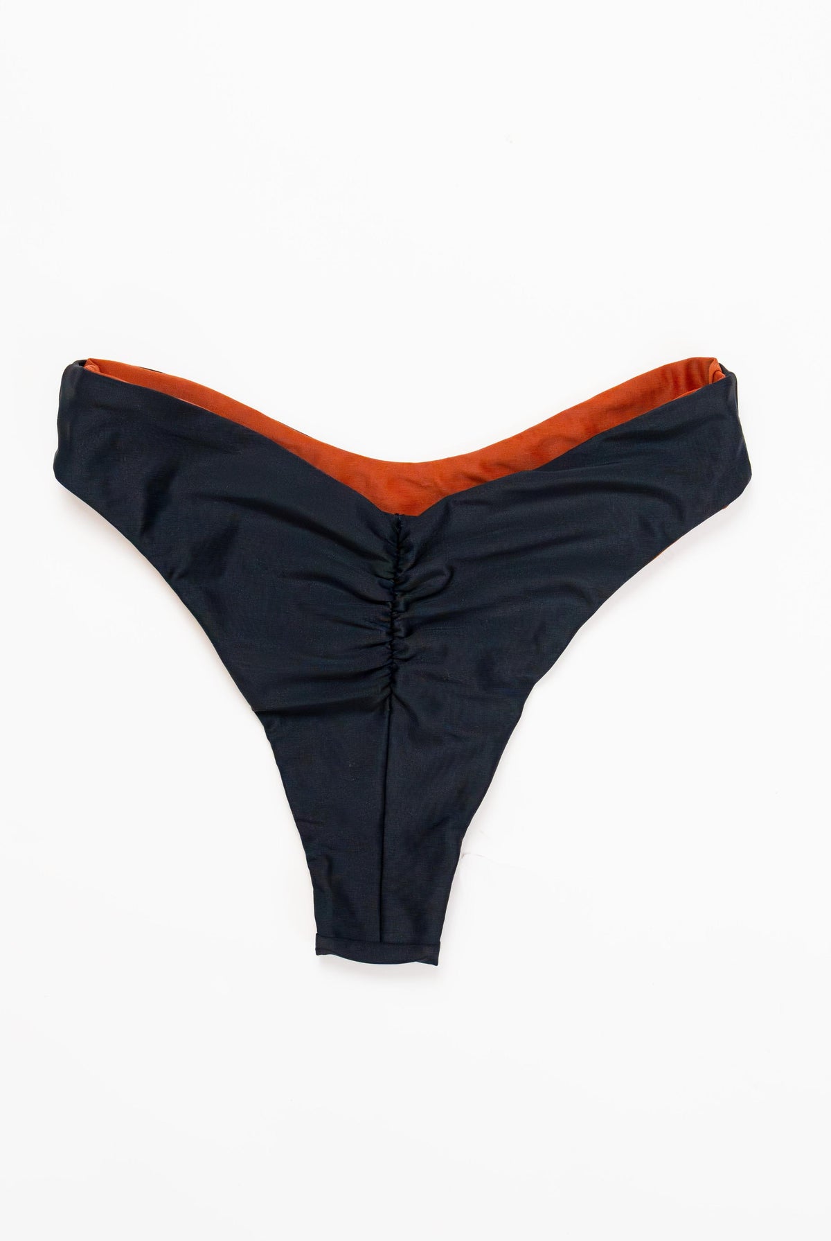 Flat lay of the Duo reversible bikini bottom in Midnight with the Sand side showing at the edge