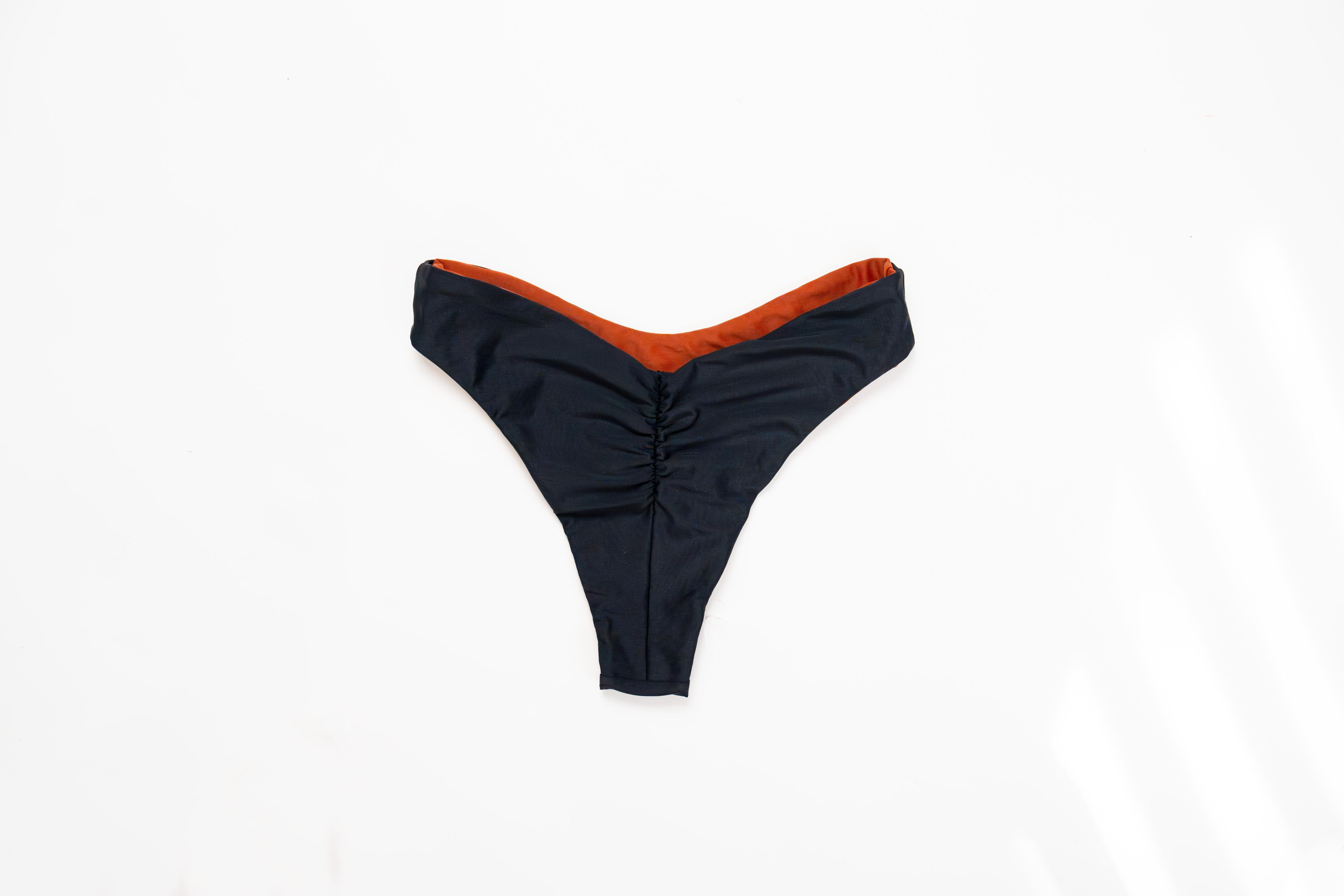 Flat lay of the Duo reversible bikini bottom in Midnight with the Sand side showing at the edge